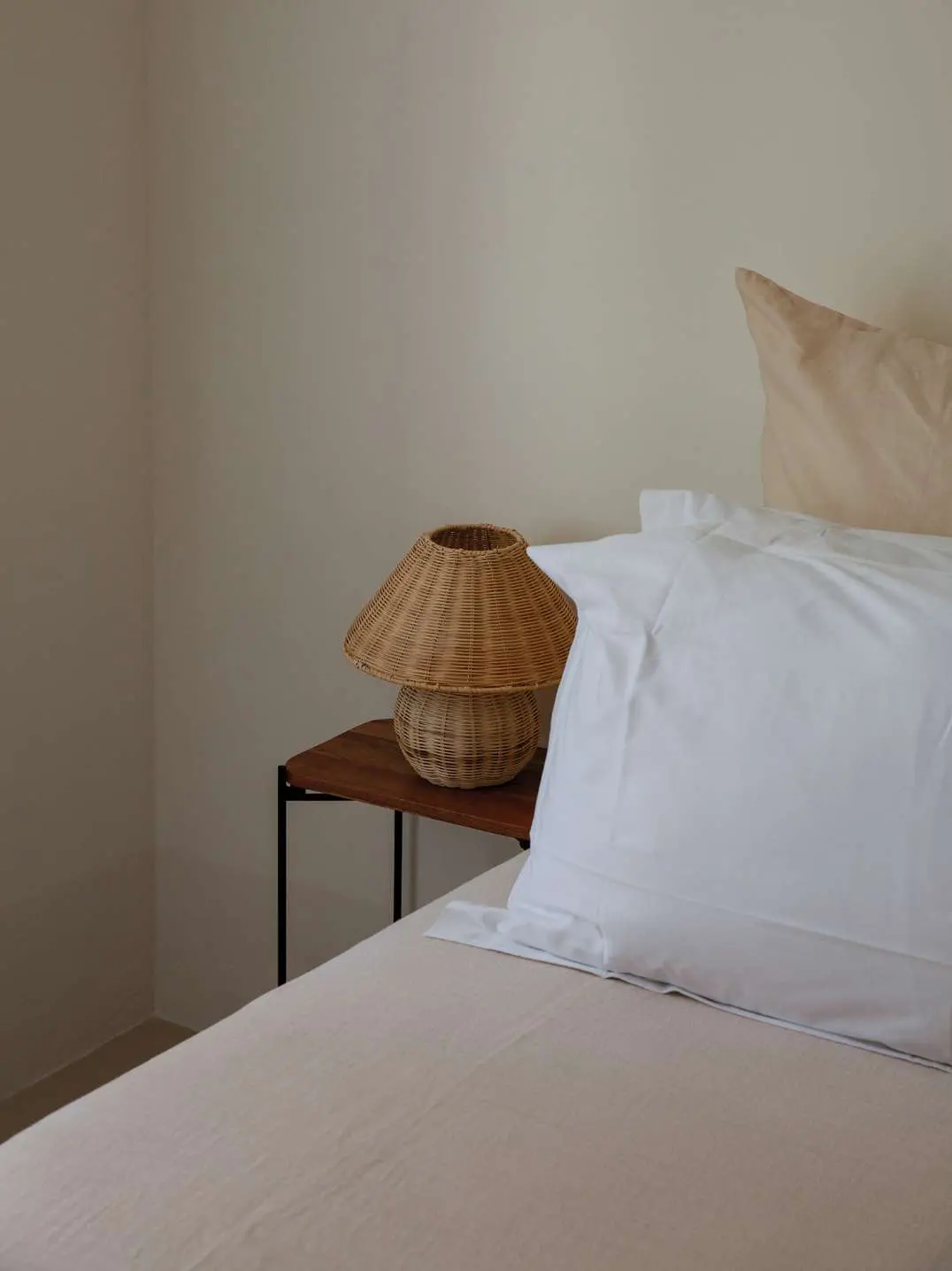 Uma cama feita com roupa branca de linho e um candeeiro de ratã na mesa de cabeceira