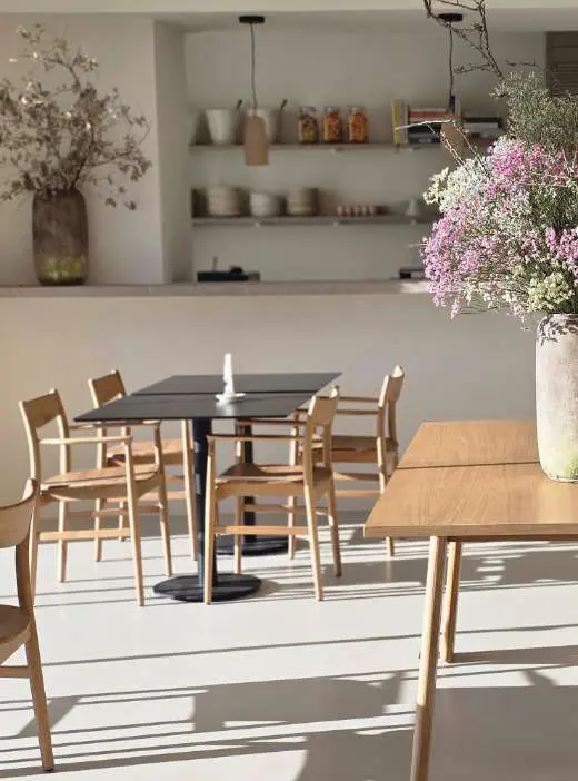 A sala de jantar da cozinha: prateleiras abertas, mesas de carvalho claro e jarras altas de flores secas