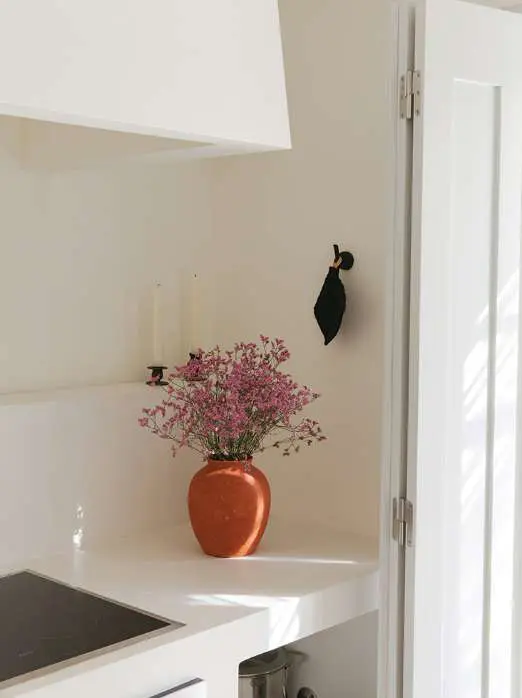 Flores cor-de-rosa numa jarra de barro sobre uma bancada branca de cozinha