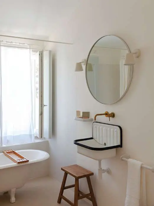 Uma casa de banho com banheira de patas, um espelho redondo e uma torneira de latão junto à janela