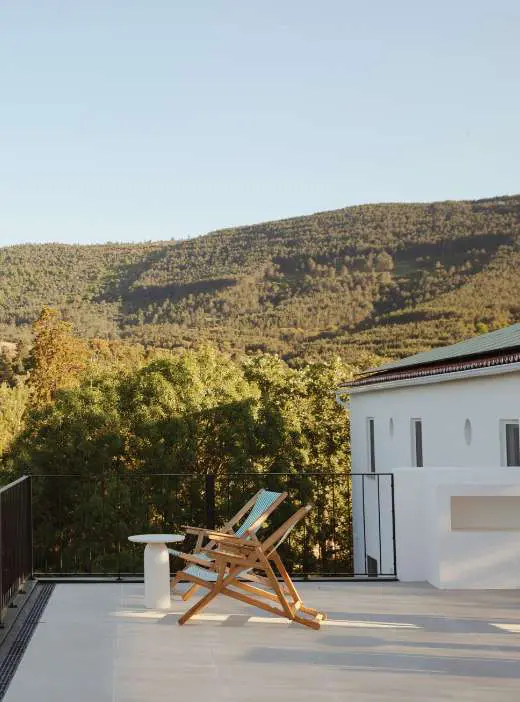 Uma espreguiçadeira de madeira no terraço, sobre as encostas arborizadas da serra