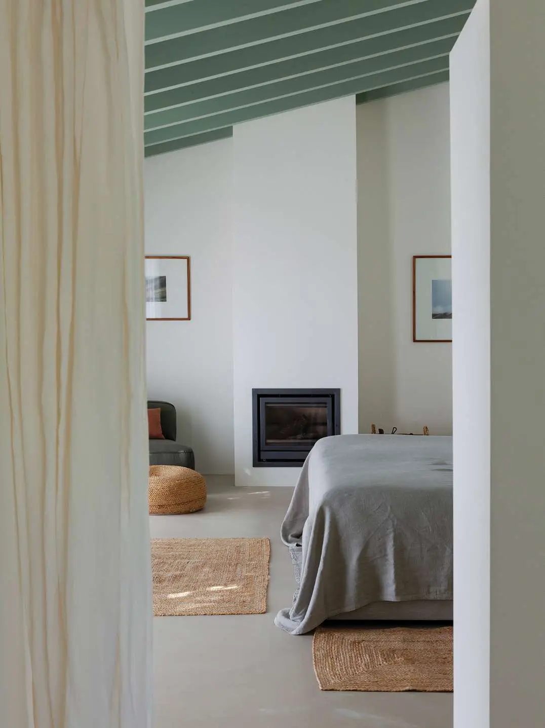 Um quarto visto através de uma cortina de linho, com lareira e uma colcha cinzenta