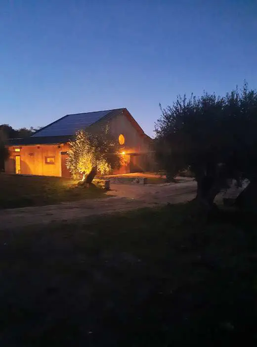 O celeiro iluminado por dentro ao anoitecer, as janelas quentes contra o céu azul-escuro
