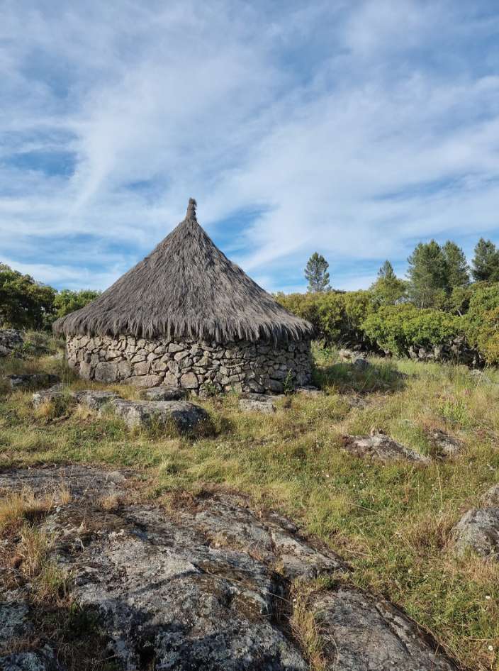 Uma choça redonda de pedra com telhado de colmo, entre rochas de granito